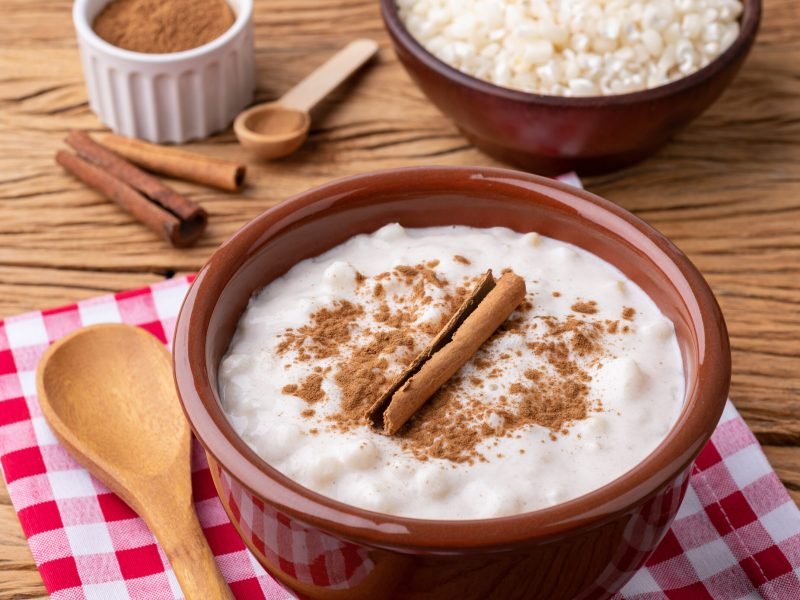 Canjica or munguza, typical brazilian white corn sweet cream wit Canjica or munguza, typical brazilian white corn sweet cream with cinnamon over wooden table.